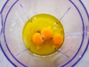Some eggs, sugar, and oil sit in a blender