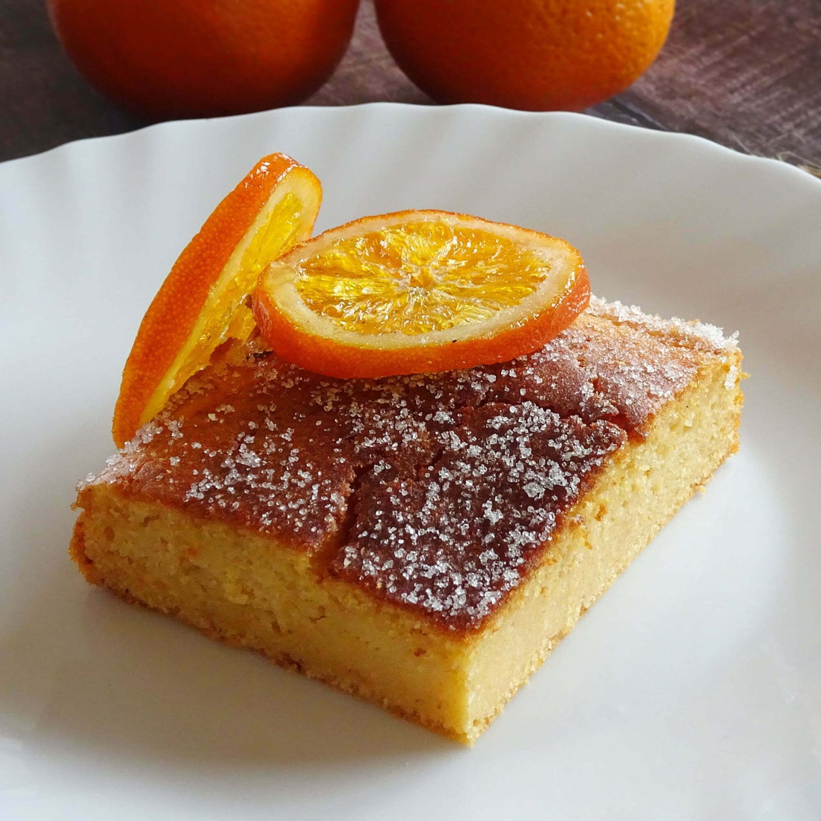 A slice of orange and grapefruit cake sits on a white plate and is garnished with a slice of candied orange