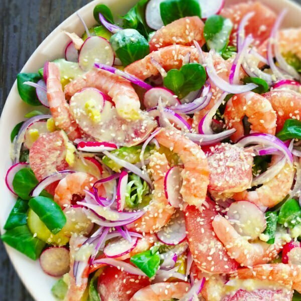 A round plate sit on a wooden counter full of color shrimp avocado salad