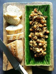 A large green dish sits on a chopping board with a serving of spinach with chickpeas, beside a loaf of sliced white bread