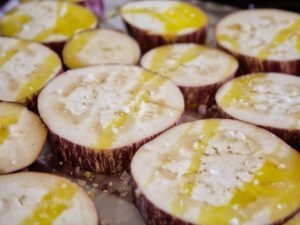Slices of eggplant are arranged on a baking tray and covered with olive oil and some sea salt flakes.