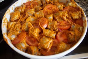 a large casserole dish with some fish fillets, tomatoes, red onion, and romesco sauce mixed together.