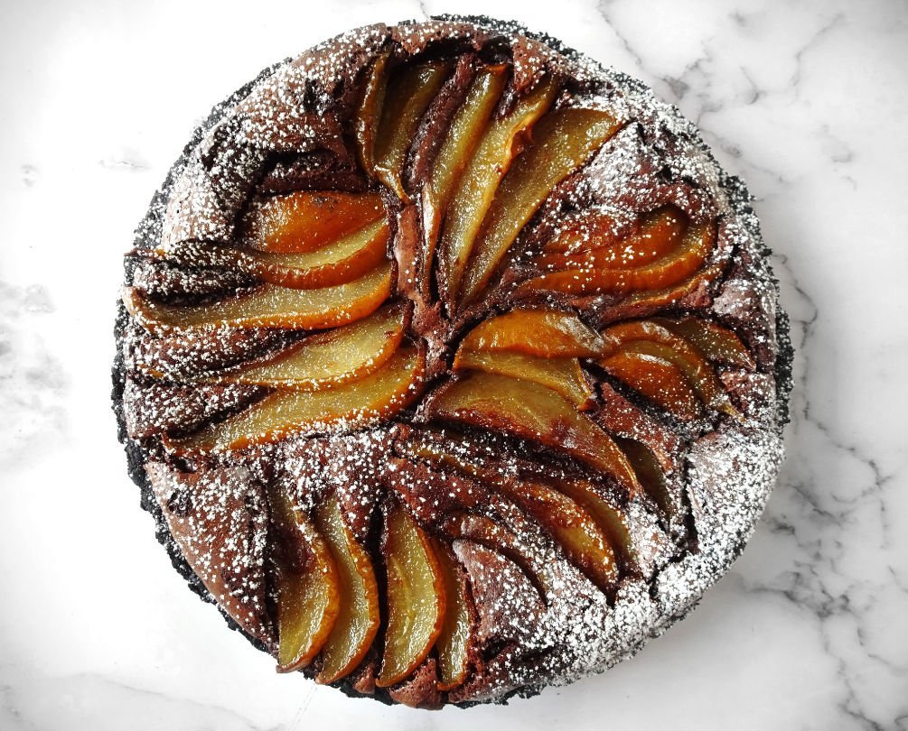 A chocolate and pear tart sits on a white marble countertop 