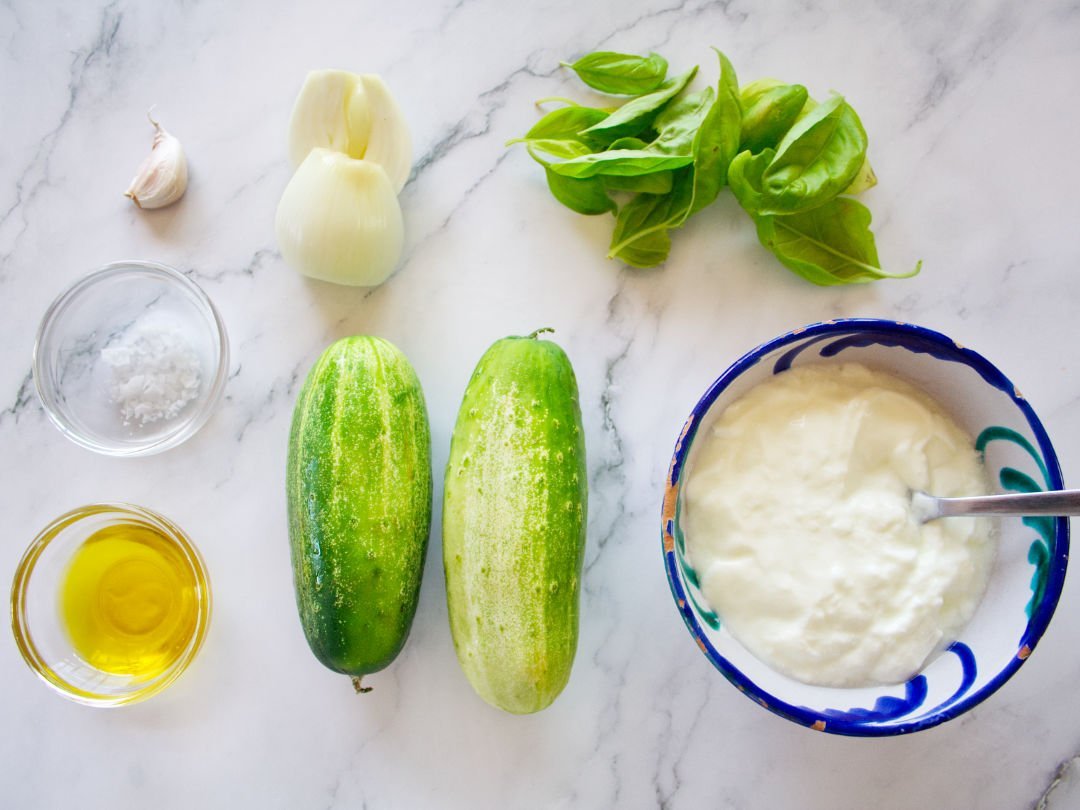 ingredients used to make cold cucumber soup are laid out on a white marble counter