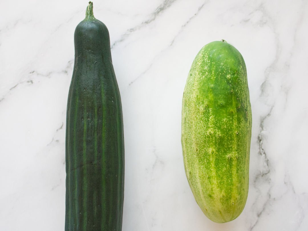 an English cucumber and a Spanish cucumber sit side by side on a white marble counter