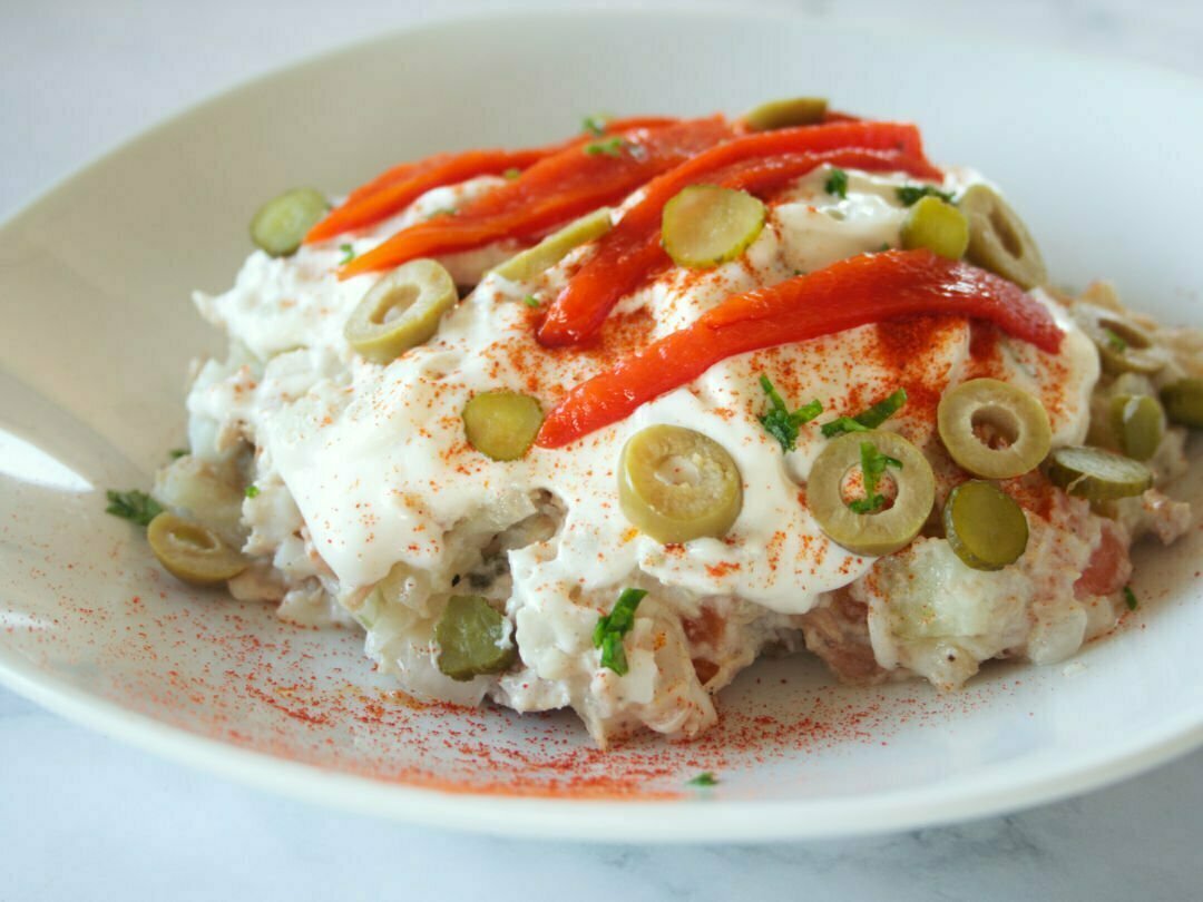 a plate of ensalada rusa is garnished with a few strips of roasted pepper