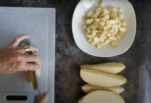 two hands are chopping up some potato on a large white chopping board.