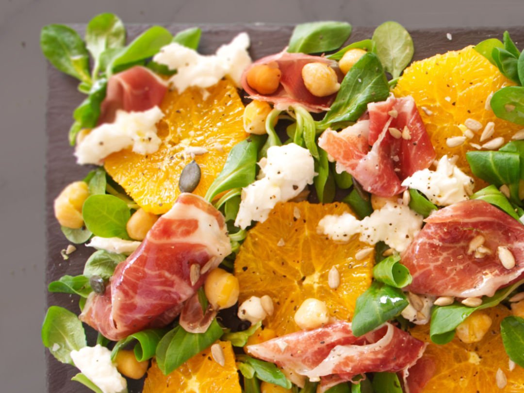 A large platter of jamon iberico sald sits topped with mozarella, salad greens, chickpeas, and seasoned with salt and pepper