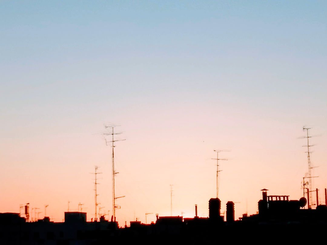 shilouettes of antennas sit on building rooftops at sunset