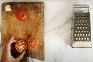 a large rustic chopping board hold some sliced tomatoes and a few cloves of garlic