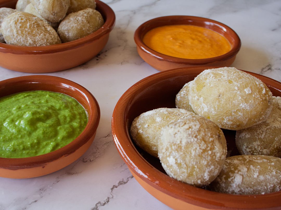 Small earthenware dishes filled with papas arrugadas, green mojo, and red mojo sauces.