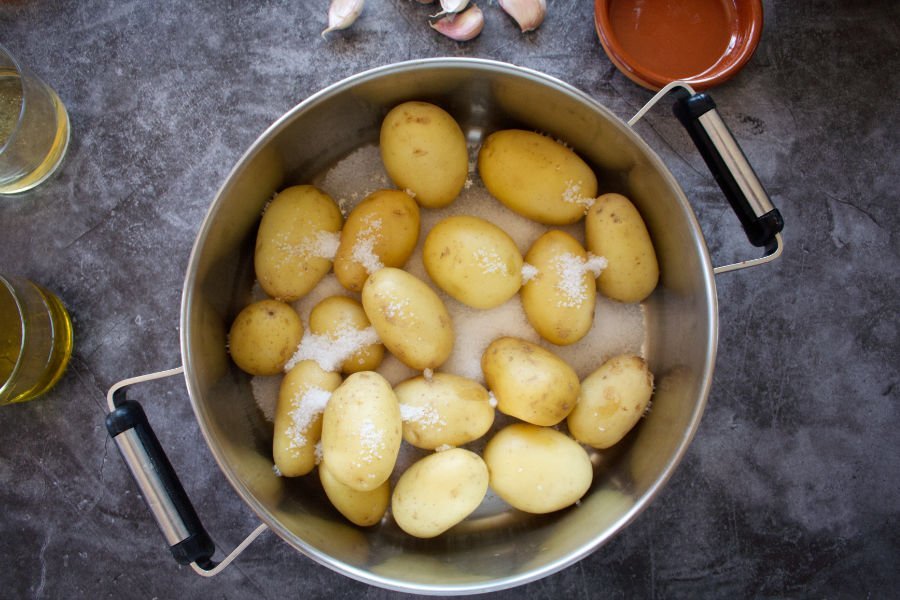 A large pot sits with some potatoes and salt