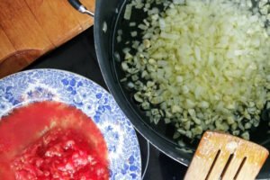 a large pot cooks some onion and garlic beside some tomato salsa