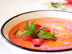 A small ceramic bowl sits filled with water melon gazpacho that has been garnished with a few sprigs of mint