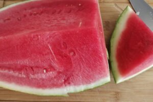 a large piece of watermelon is being sliced on a wooden chopping board