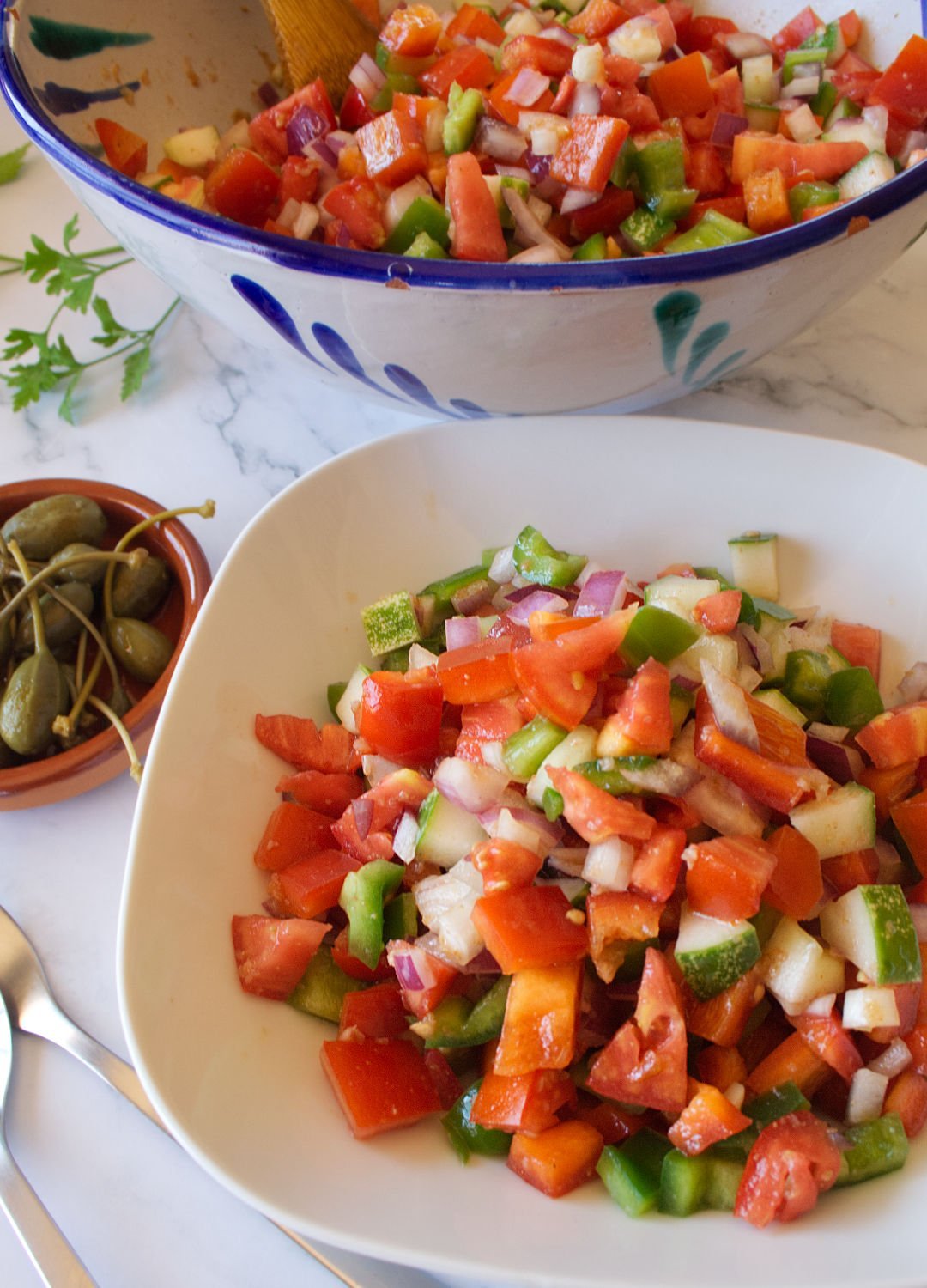 A large colorful bowl of Pipirrana Spanish Salad sits waiting to be served to a small white bowl.