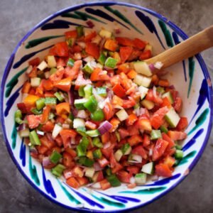 Some Pipirrana Spanish salad sits in a colorful bowl on a grey slate counter.