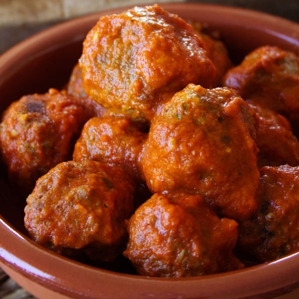 A small ceramic bowl of Albondigas sits in a rich sofrito sauce waiting to be served