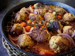 A large pan of vegetarian meatballs sits garnished with cherry tomatoes and thin slices of red onion