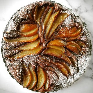 A chocolate and pear tart is decorated with slices of pear and dusted with some icing sugar.