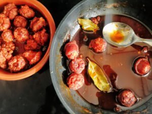 A frying pan sits with chorizo cooked in cider being served into a small earthernware dish