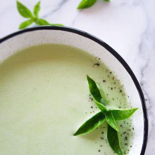 a bowl of cucmuber soup is garnished with a few sprigs of fresh basil.