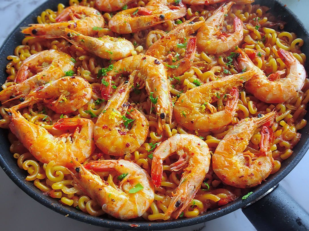 a large pan of fideua marisco sits topped with large prawns and some parsley