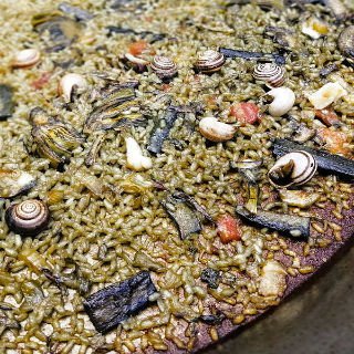 A large pan of Orchard paella sits with small snails and roasted vegiies scattered on top