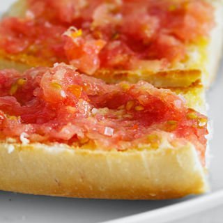 a few slices of pan con tomate sit on a plate garnished with sea salt and olive oil