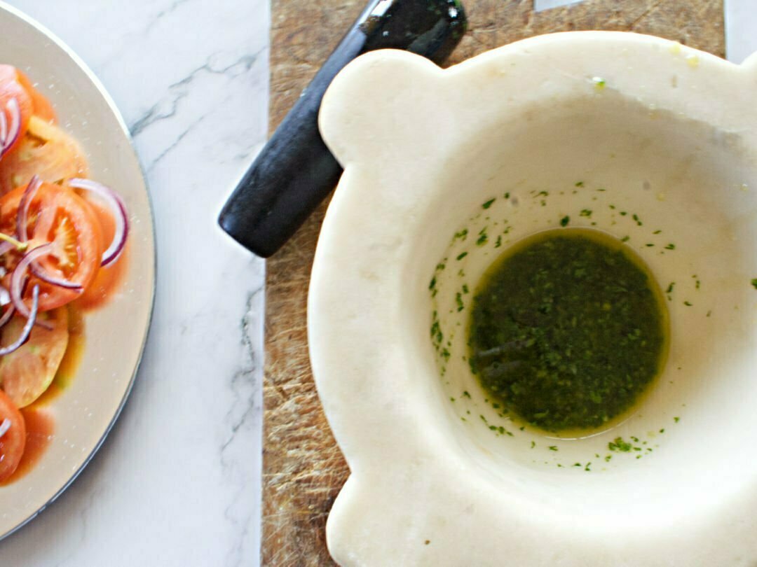 A large white marble mortar sits with some homemade green pesto in the bottom.