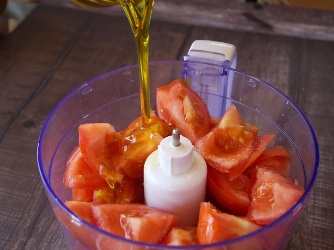 Olive oil is poured on top of some diced tomatoes in a blender