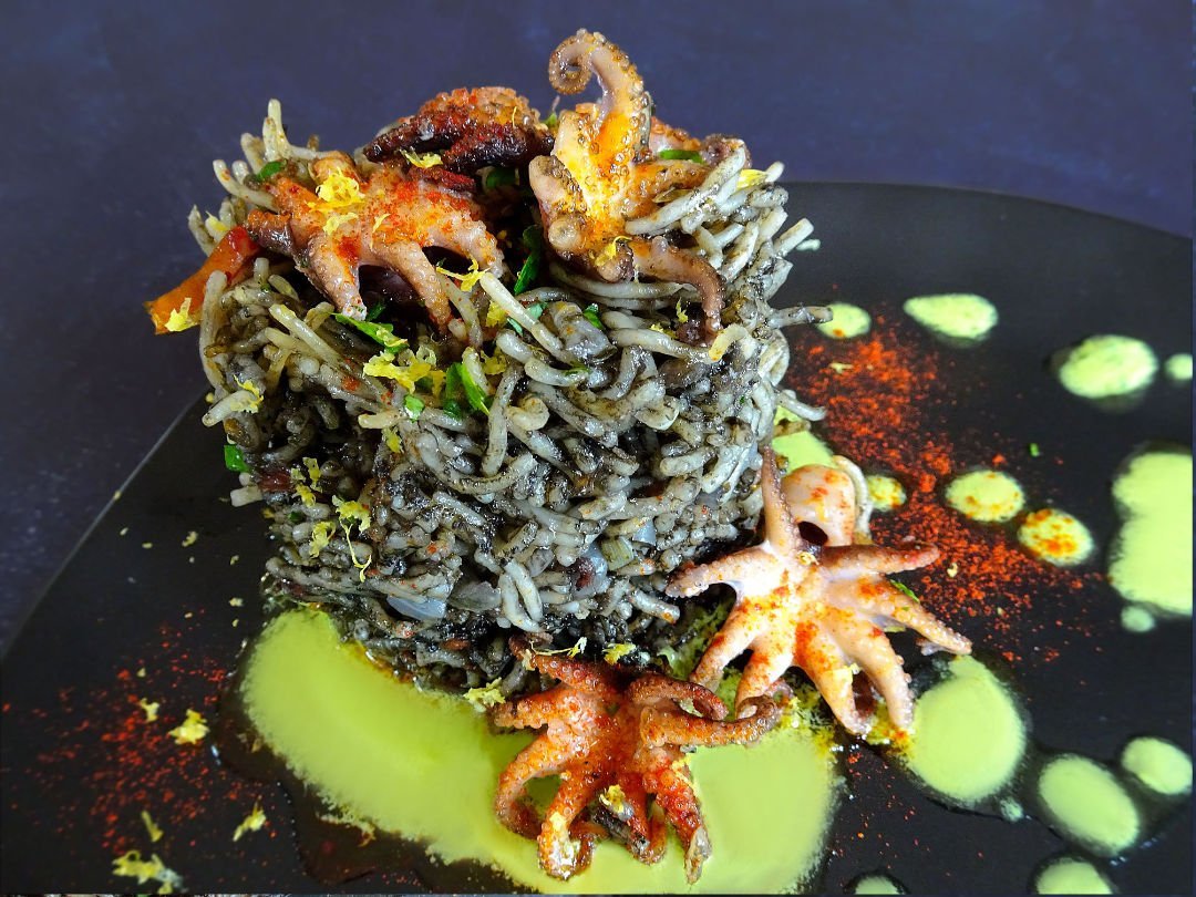 A tall stacck of squid ink pasta sits beside a few cooked baby octopus