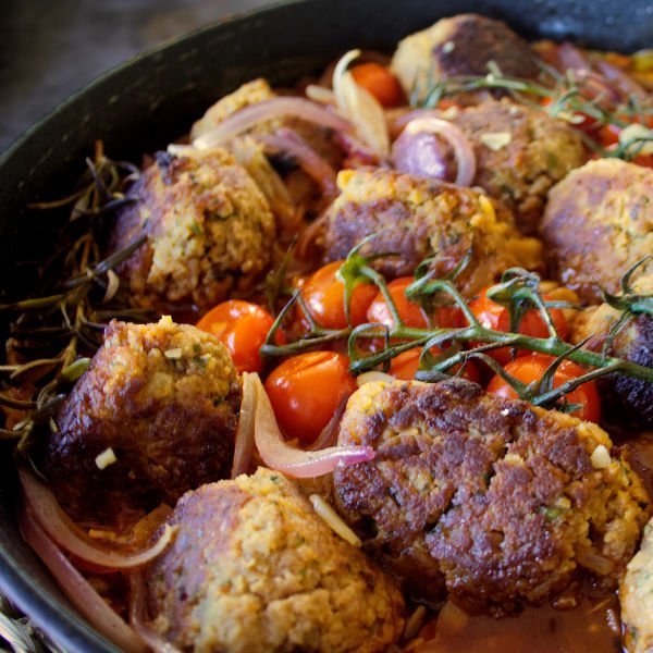 A large pan of vegetarian meatballs sits garnished with cherry tomatoes and thin slices of red onion