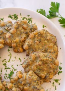 Oven-baked chickpea fritters sit on a white plate with a sprinkling of chopped parsley