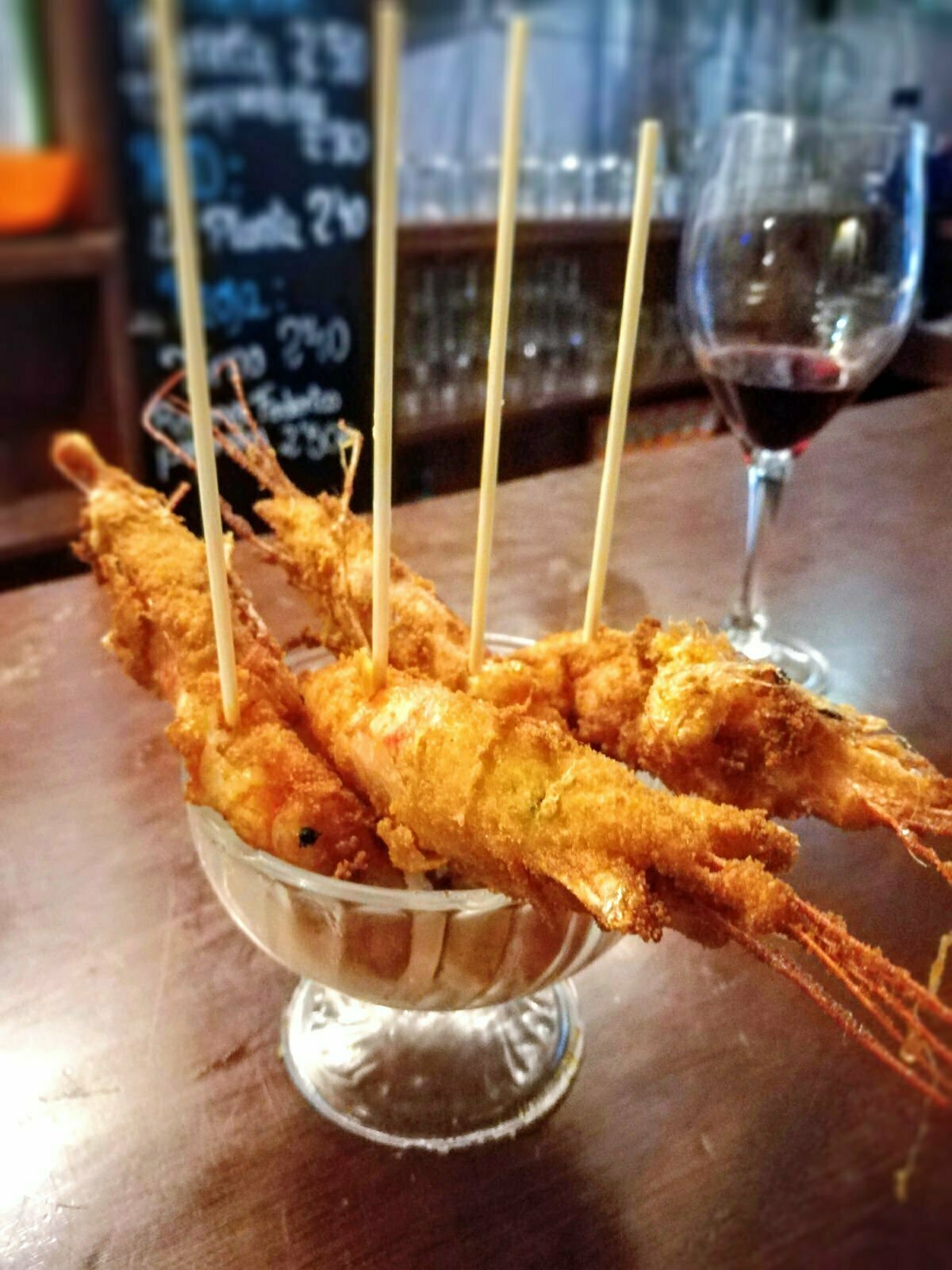 a small glass bowl of fried shrimp with large sticks poking out on top