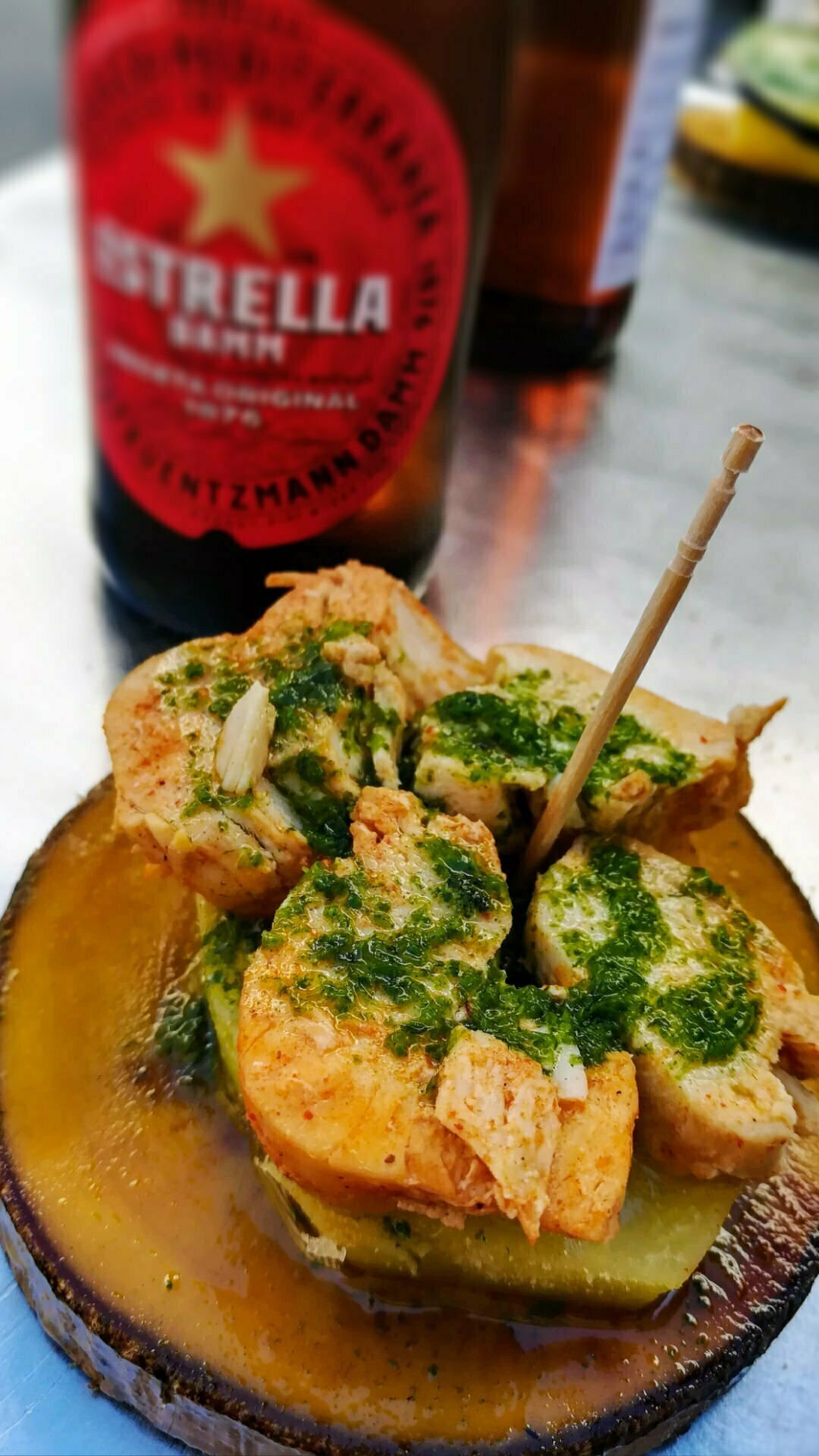  aplate of fried fish with a green sauce sits beside a bottle of beer
