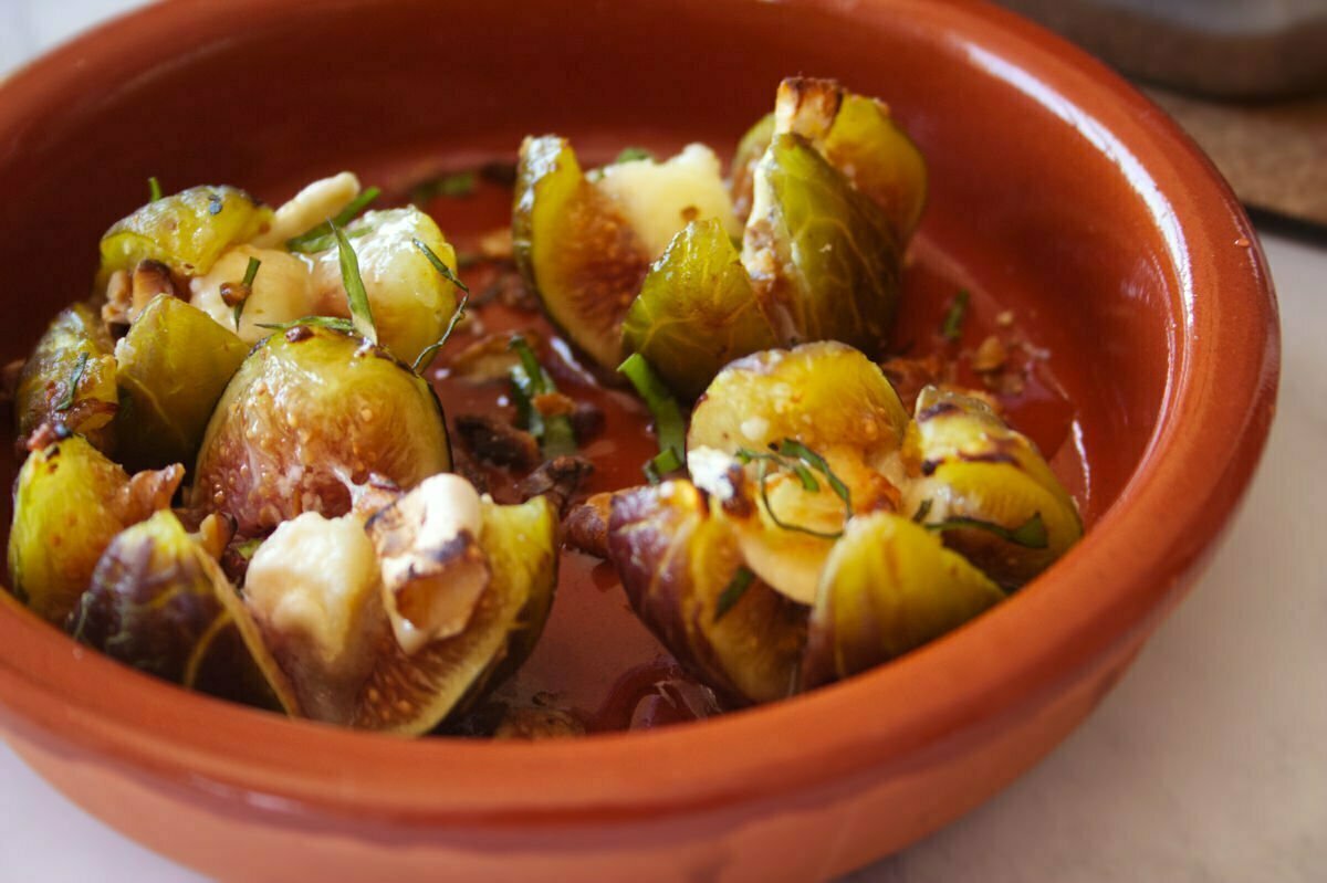 A small earthenware bowl holds some grilled figs with goat's cheese, honey and toasted walnuts on top. 