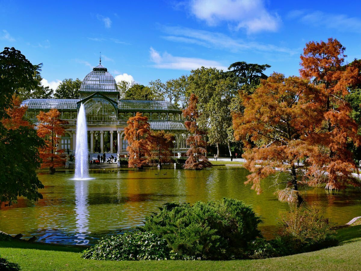 a view over a lake to a large glasshouse structure in retiro park.