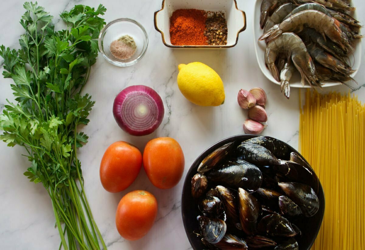 ingredients are laid out for shrimp snd mussels pasta on a white marble counter top