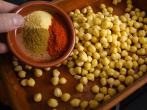 A person adds spices to a tray of prepapred chickpeas.