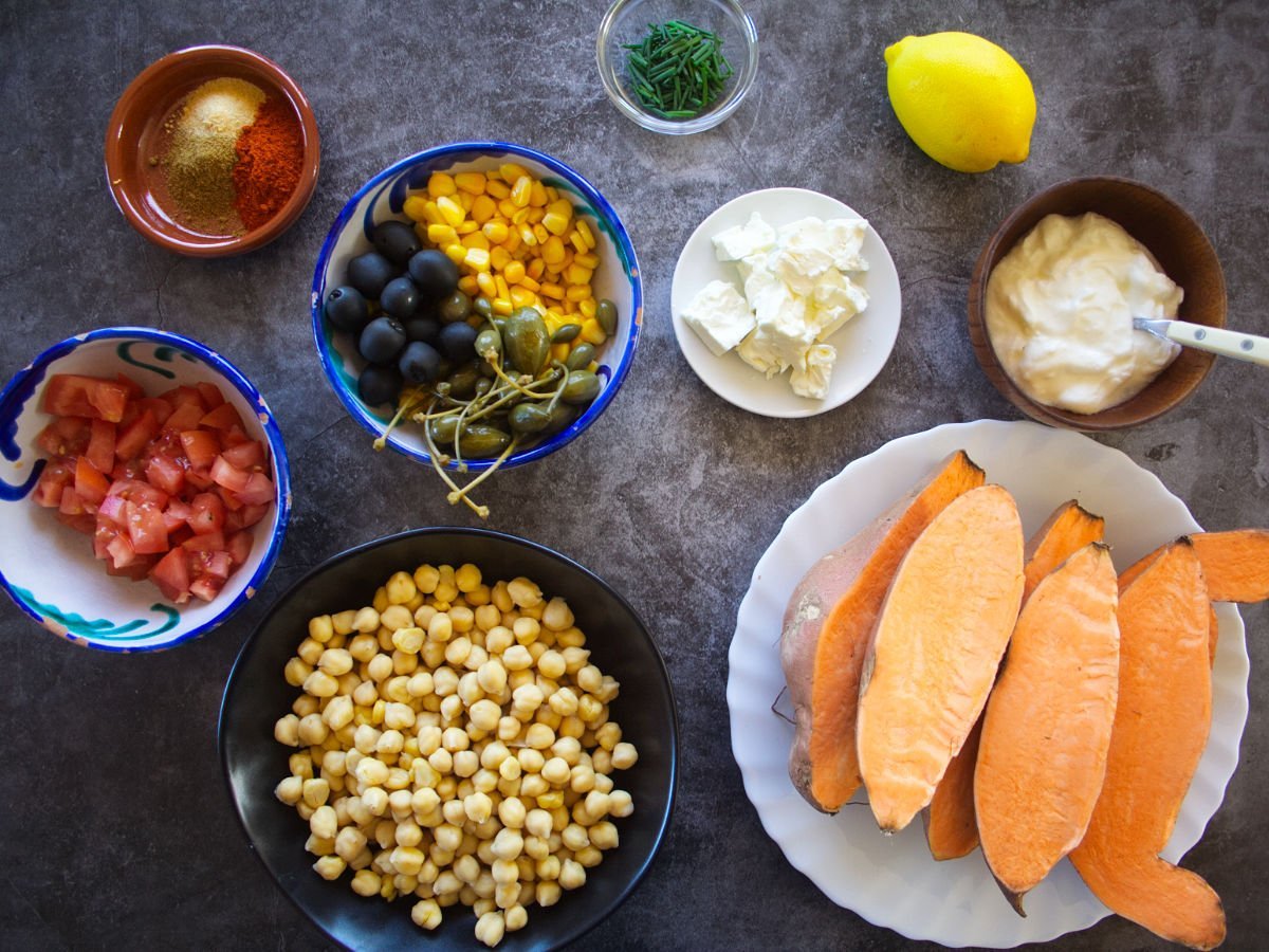ingredients for Mediterranean baked sweet potatoes are laid out on a dark stone countertop