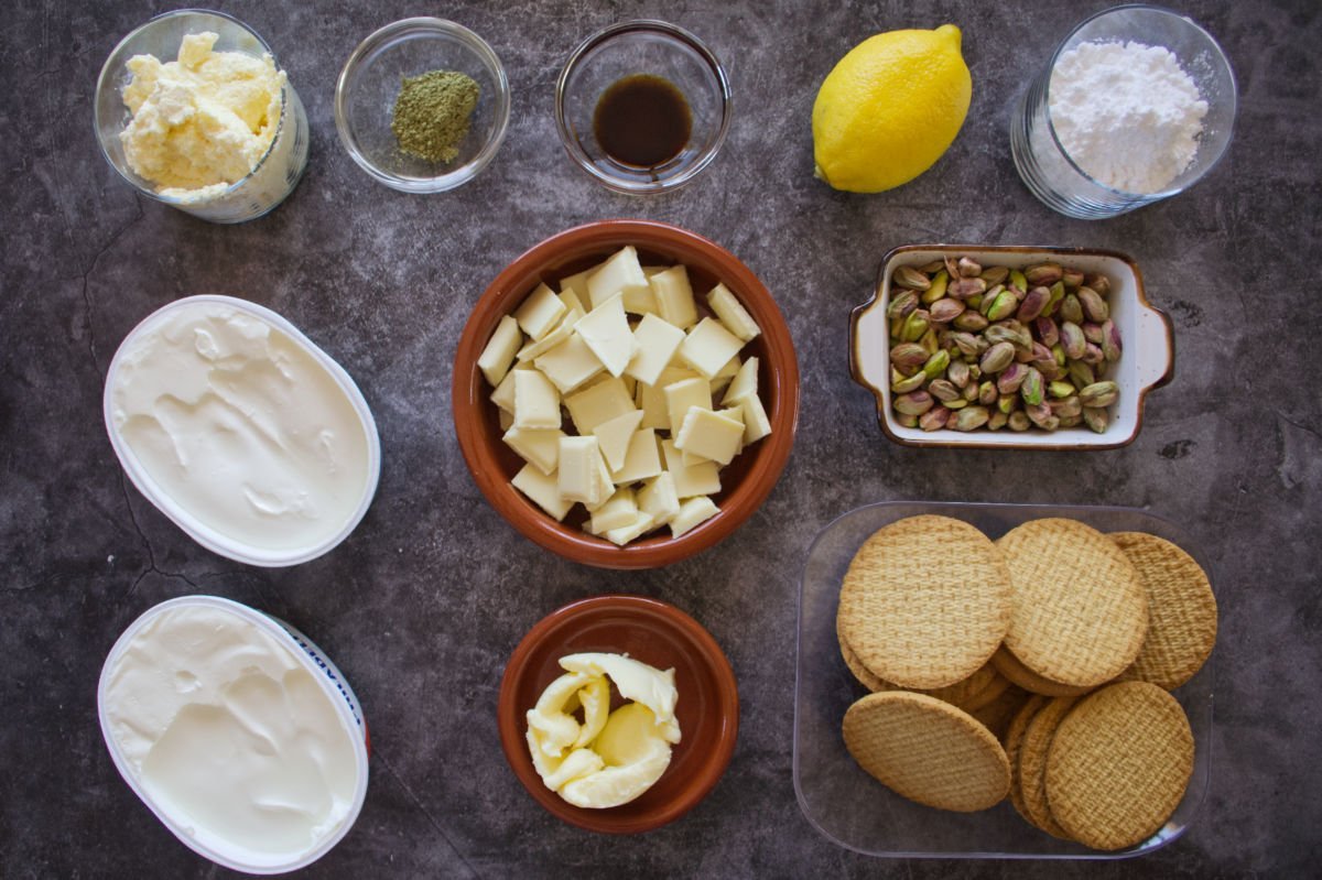 ingredients for making a white chocolate cheesecake with pistachio nuts are laid out on a dark granite counter