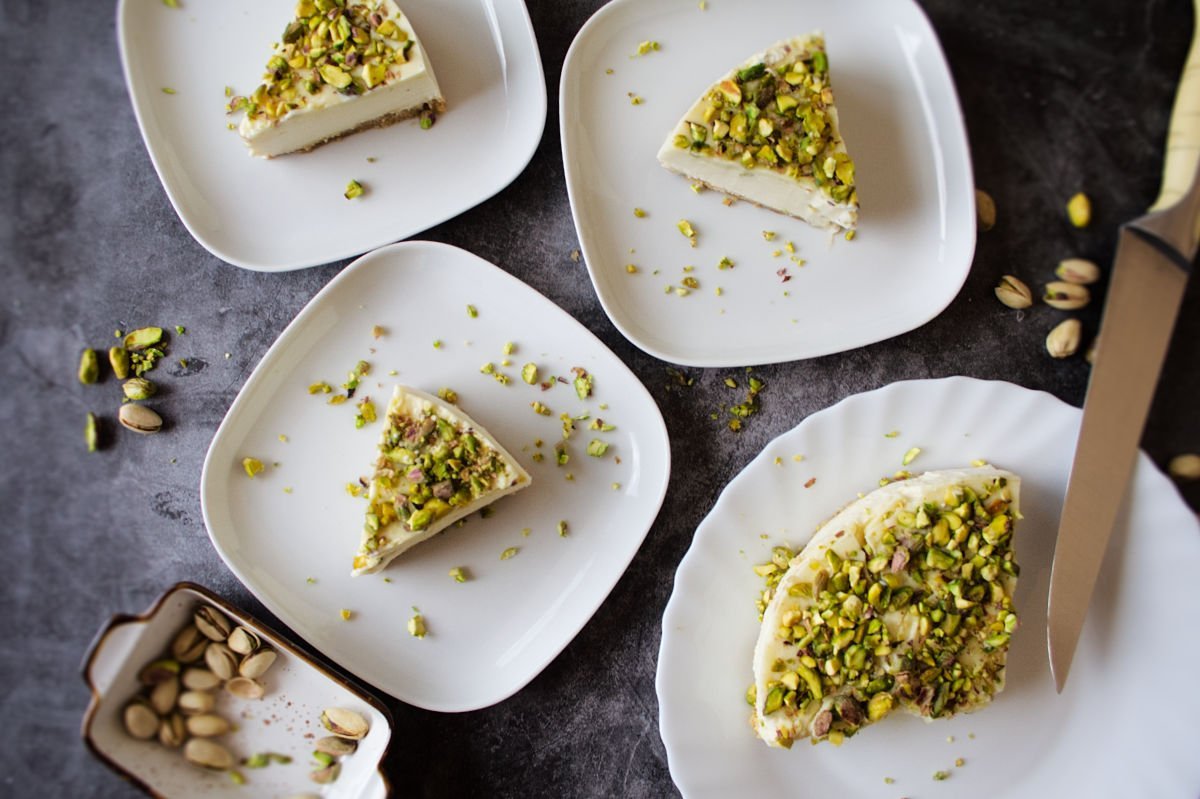 Slices of white chocolate cheesecake with pistachio crust sit on a few. plates waiting to be served.