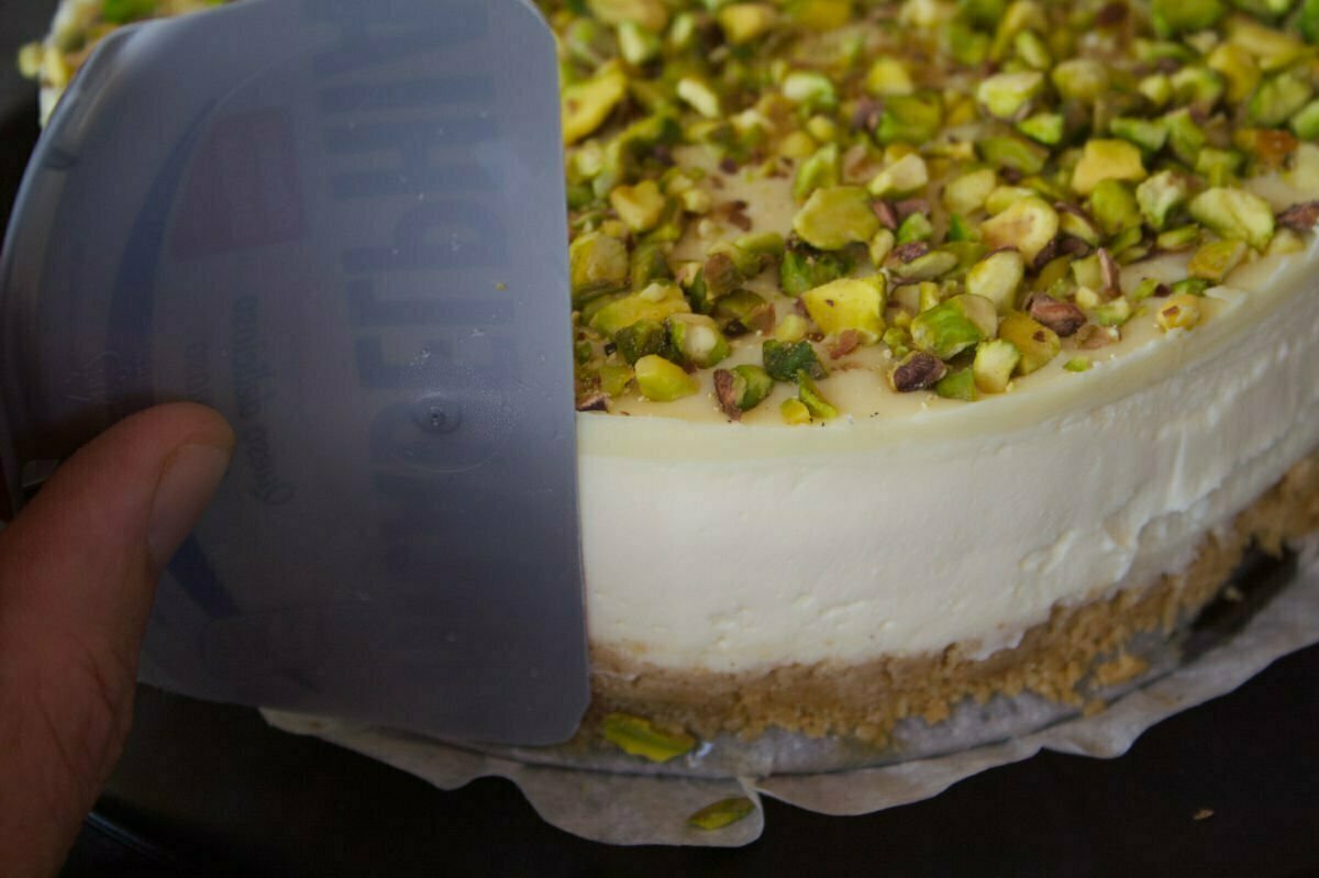 a plastic smoothing tool is used to smooth the edges of a white chocolate cheesecake