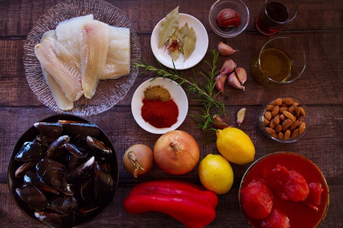 Ingredients for making Mediterranean fish stew (Zarzuela de Mariscos) are laid out on a wooden table