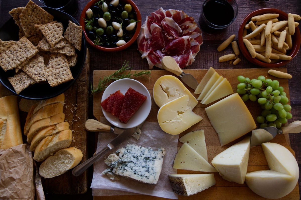 A Spain cheese bboard sits with various types of. Spanish cheese, jamon, and other snacks