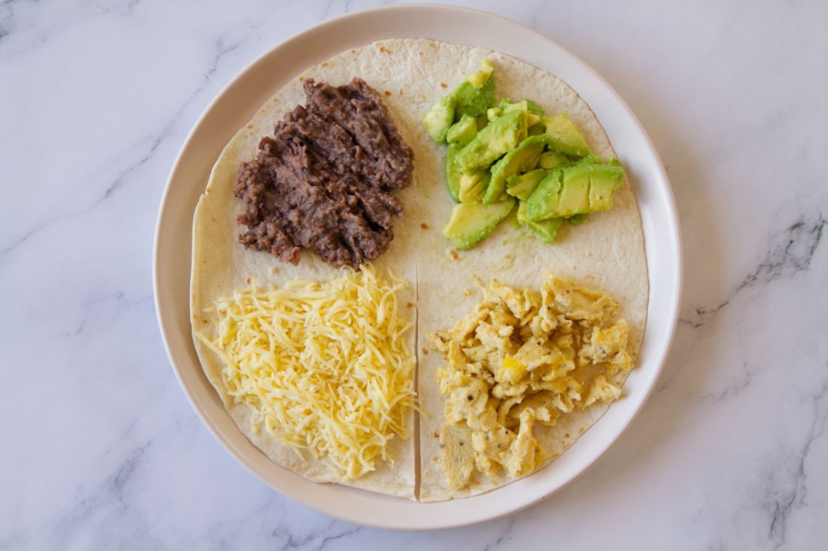 a tortilla wrap is laid out with 4 different toppings in each quarter.