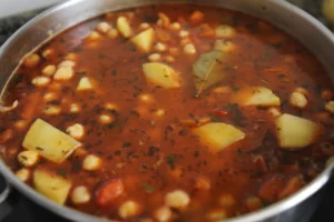 potoatoes, chickpeas, bay leaves, and vegetable stock are added to simmering vegetables and spices