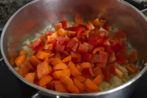 Chopped vegetables added to a pan of fried onions