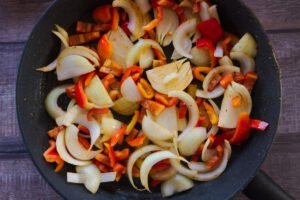 Some onion and red pepper cook in a frying pan